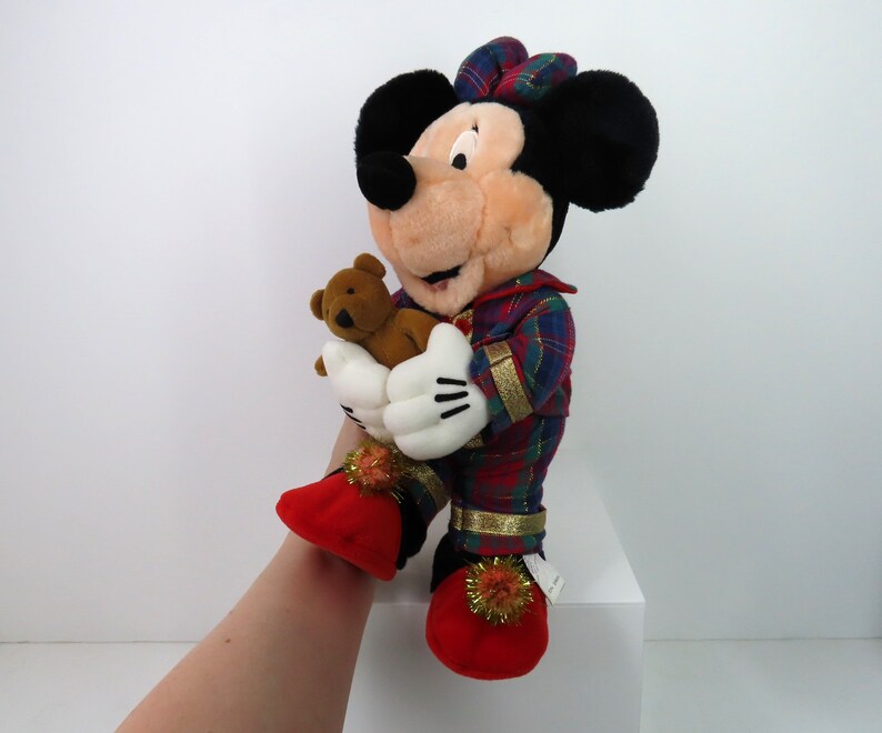 May include: A plush Mickey Mouse wearing red and green plaid pajamas and holding a brown teddy bear. He is wearing red slippers with gold trim and white pom-poms.