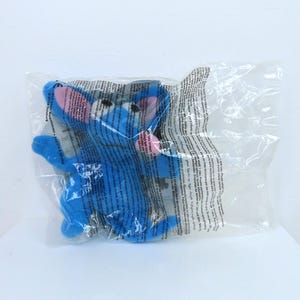 May include: A blue plush toy of a cartoon character with large ears, a pink nose, and black eyes, sealed in a clear plastic bag. The toy has a soft, fuzzy texture and is designed to resemble a friendly creature.