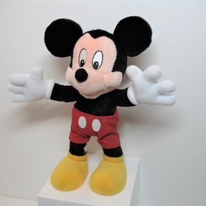 May include: A plush Mickey Mouse toy with black ears, a red and white polka dot shirt, and yellow shoes. The toy is standing on a white surface.