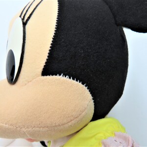 Puede incluir: Primer plano de un rat&oacute;n de peluche con orejas negras, ojos grandes y cara rosa. El rat&oacute;n lleva un vestido amarillo y rosa.