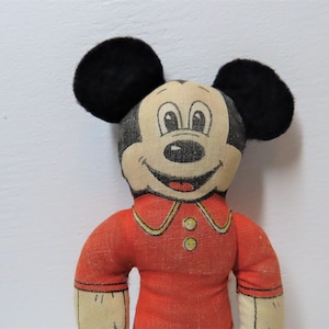 K&ouml;nnte beinhalten: Vintage Pl&uuml;schtier Mickey Mouse mit schwarzen Ohren, einem roten Shirt mit gelben Kn&ouml;pfen und einem l&auml;chelnden Gesicht.