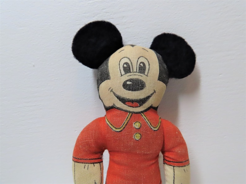 K&ouml;nnte beinhalten: Vintage Pl&uuml;schtier Mickey Mouse mit schwarzen Ohren, einem roten Shirt mit gelben Kn&ouml;pfen und einem l&auml;chelnden Gesicht.