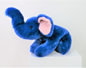 May include: A blue plush elephant toy with pink ears. The elephant is sitting on a white surface.