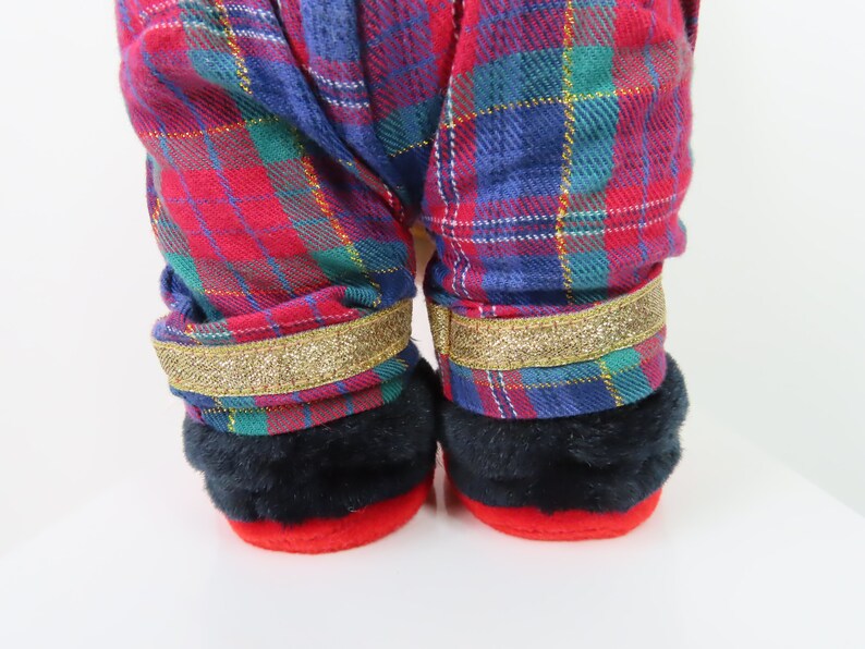 May include: Red and blue plaid pajama pants with gold glitter trim. The pants have black fur cuffs.
