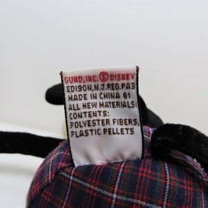 May include: A red, black, and white plaid stuffed toy with a black and white tail. The toy has a tag that reads "GUND, INC. DISNEY EDISON, N.J. REG. PA3 MADE IN CHINA 61 ALL NEW MATERIALS CONTENTS: POLYESTER FIBERS, PLASTIC PELLETS".