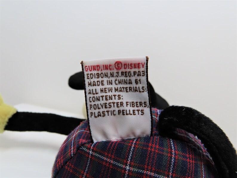 May include: A red, black, and white plaid stuffed toy with a black and white tail. The toy has a tag that reads "GUND, INC. DISNEY EDISON, N.J. REG. PA3 MADE IN CHINA 61 ALL NEW MATERIALS CONTENTS: POLYESTER FIBERS, PLASTIC PELLETS".