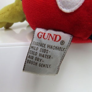 May include: A white tag with the word "GUND" in red lettering and the text "Surface Washable, Mild Suds, Cold Water, Air Dry, Brush Gently."
