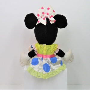 Puede incluir: Un juguete de peluche de Minnie Mouse con un vestido amarillo con lunares azules y un lazo rosa con lunares blancos.