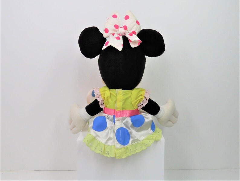 Puede incluir: Un juguete de peluche de Minnie Mouse con un vestido amarillo con lunares azules y un lazo rosa con lunares blancos.