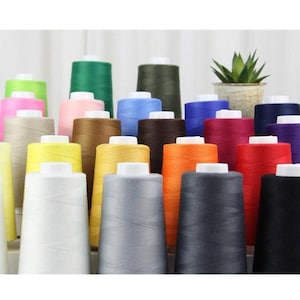 May include: A collection of 24 spools of thread in various colors, including white, black, red, blue, green, yellow, orange, brown, and beige. The spools are arranged in rows and are all the same size.