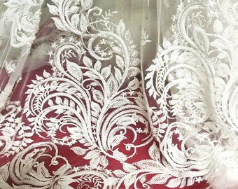 May include: White lace fabric with a delicate floral pattern. The lace is sheer and has a soft, flowing texture.