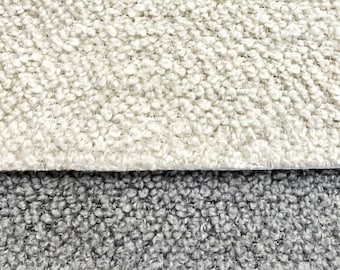May include: Close-up of two fabric swatches. The top swatch is a light cream color with a textured, fuzzy surface. The bottom swatch is a dark gray with a similar textured surface.