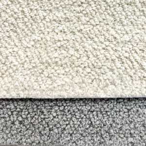 May include: Close-up of two fabric swatches. The top swatch is a light cream color with a textured, fuzzy surface. The bottom swatch is a dark gray with a similar textured surface.
