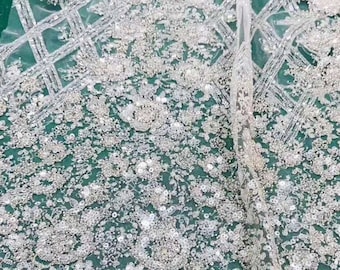 May include: White beaded fabric with a delicate floral pattern. The fabric is sheer and has a subtle shimmer.