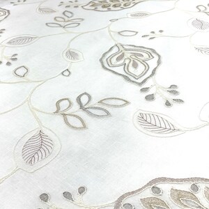 May include: White fabric with an embroidered floral pattern in shades of beige and gray. The design features delicate leaves and flowers.