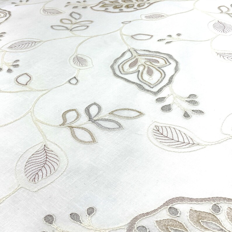 May include: White fabric with an embroidered floral pattern in shades of beige and gray. The design features delicate leaves and flowers.