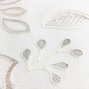 May include: White fabric with embroidered floral designs in shades of brown and gray. The design features leaves and stems.