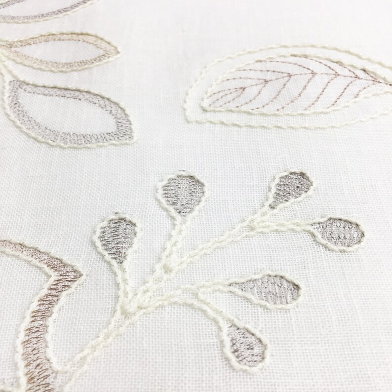 May include: White fabric with embroidered floral designs in shades of brown and gray. The design features leaves and stems.