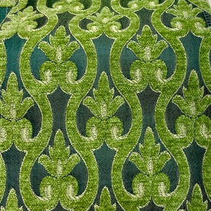 May include: Close-up of a green patterned fabric. The design features a repeating pattern of stylized floral shapes in a lighter green, set against a darker green background. The fabric has a textured, plush appearance.