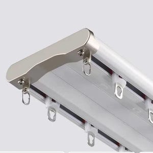 Può includere: Primo piano di un sistema di binario per tende bianco con una parte superiore in metallo argentato e anelli di sospensione. Il binario ha più scanalature parallele e ganci di plastica bianca per fissare le tende.