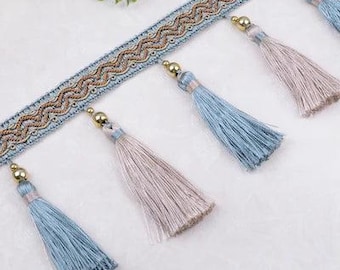 May include: Decorative trim featuring a light blue and gold woven ribbon with a wavy pattern. Attached are alternating blue and taupe tassels with gold-colored caps. This trim is suitable for various craft projects.