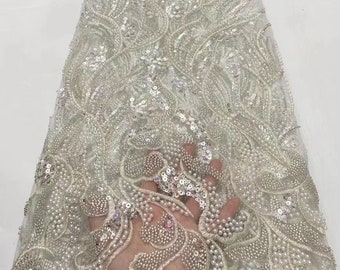 May include: White beaded and sequined lace fabric with a floral pattern. The fabric is sheer and delicate, with a soft, flowing texture.