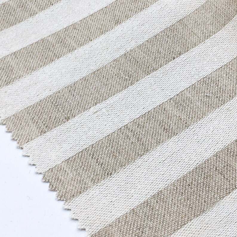 May include: Close-up of a beige and white striped fabric with a diagonal pattern. The fabric has a linen texture.