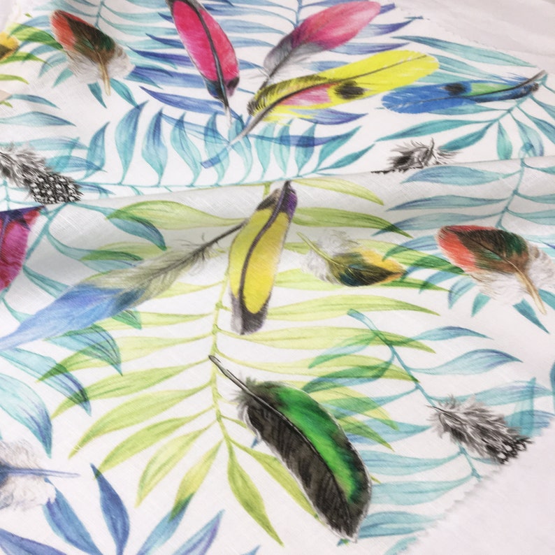 May include: White fabric with a tropical print featuring colorful feathers and green leaves.