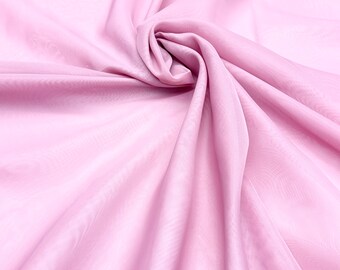 May include: A close-up shot of a light pink fabric with a soft, flowing texture. The fabric is draped and folded, creating a sense of movement and depth. The color is a delicate pastel, and the material appears to be lightweight and sheer.