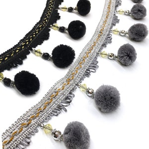 May include: Two trims with black and gray pom-poms and crystal beads. The trim on the top is black with gold accents and the trim on the bottom is silver with gold accents.