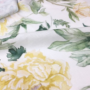 May include: White fabric with a watercolor floral pattern featuring yellow flowers and green leaves.