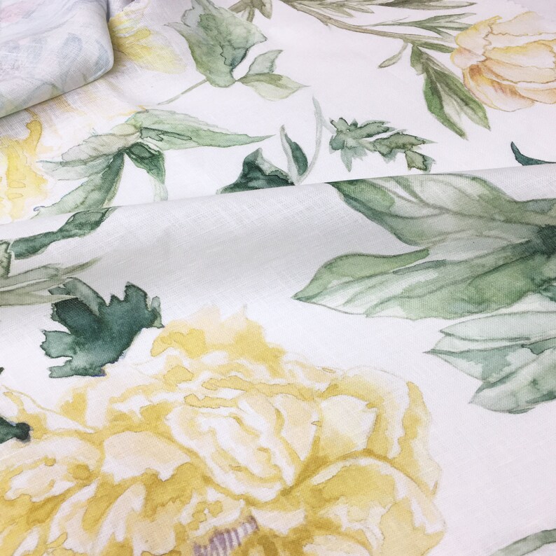 May include: White fabric with a watercolor floral pattern featuring yellow flowers and green leaves.