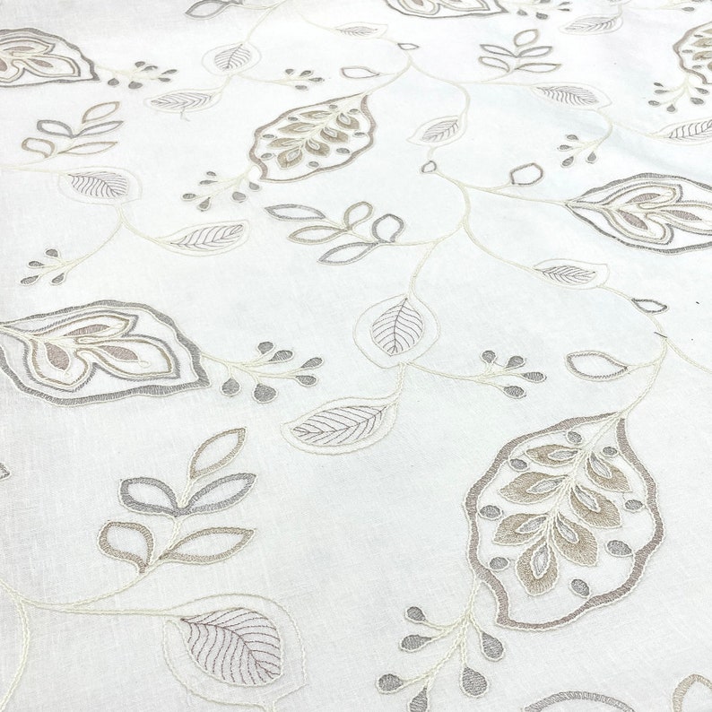 May include: White fabric with an embroidered pattern of gray and beige leaves and vines.