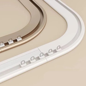 Può includere: Sezioni di binari per tende curve in oro e bianco. I binari hanno piccoli anelli distanziati uniformemente per appendere le tende. Il design è moderno e minimalista, con un focus sulla funzionalità e un'estetica pulita.