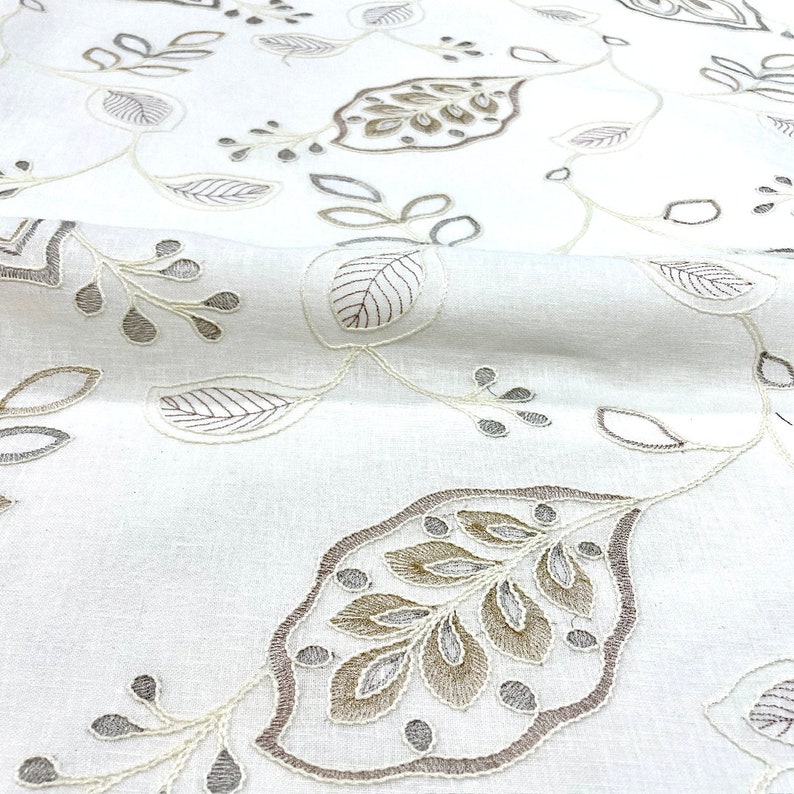 May include: White fabric with a delicate embroidered pattern of leaves in shades of brown and gray.