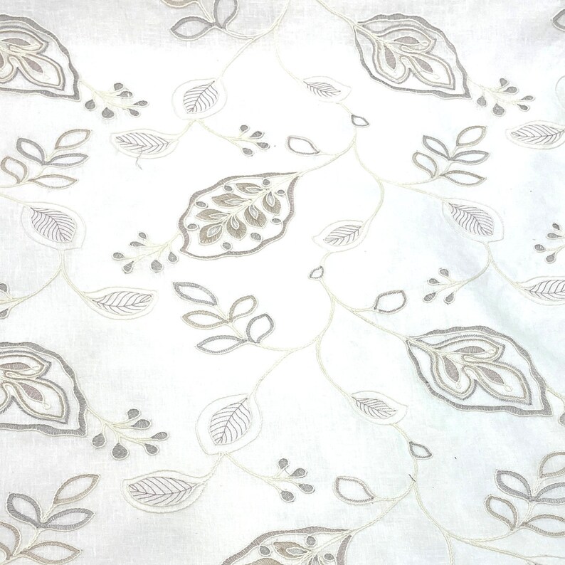 May include: White fabric with a delicate, embroidered pattern of gray leaves and vines. The design is reminiscent of a traditional floral motif.