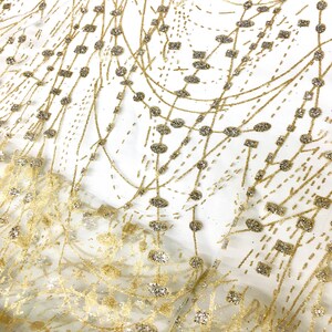 May include: Gold glitter fabric with a delicate pattern of circles and lines. The fabric has a sheer, mesh-like texture.