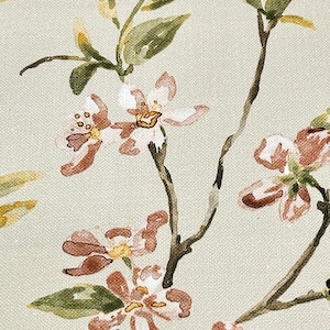 Op de afbeelding: Een close-up van een bloemenpatroon op een licht beige stof. Het patroon heeft delicate roze en witte bloemen met groene bladeren.