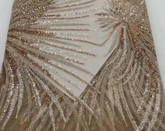 May include: A close-up of a sheer fabric with a delicate pattern of sequins and beads. The fabric is a light gold color and has a shimmery finish.