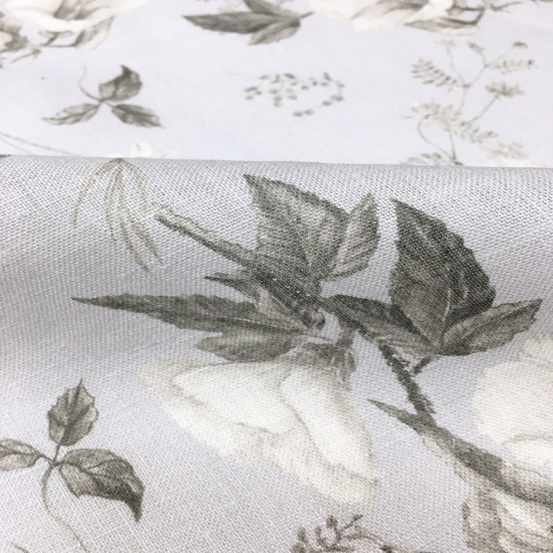 May include: A light gray fabric with a white floral pattern. The flowers are outlined in gray and have a subtle texture.