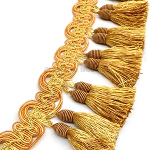 May include: Gold and brown tassel trim with a decorative woven design. The trim features a series of tassels with a looped cord detail.