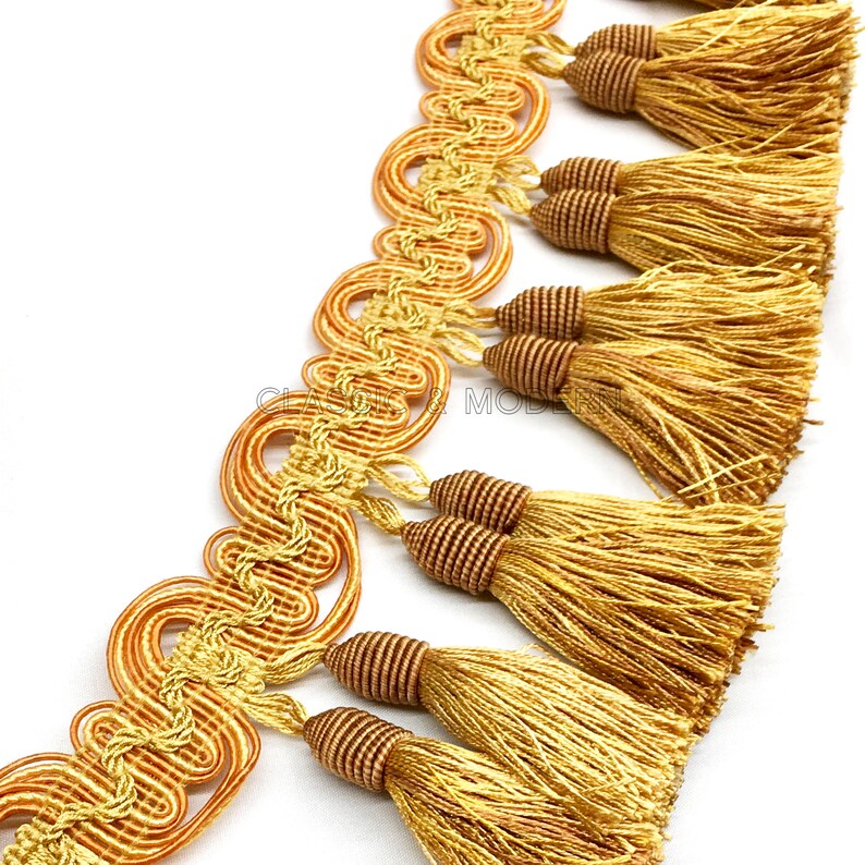 May include: Gold and brown tassel trim with a decorative woven design. The trim features a series of tassels with a looped cord detail.