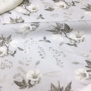 May include: A light gray fabric with a white floral pattern. The flowers are stylized and have a delicate, watercolor-like appearance. The fabric has a subtle texture.