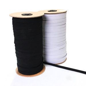 May include: Two spools of elastic cord, one black and one white, are wound around cardboard spools. The spools are sitting on a white surface.