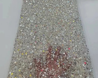 May include: White mesh fabric with iridescent sequins. The sequins are small and round, and they are densely packed together. The fabric has a shimmery, sparkly appearance.