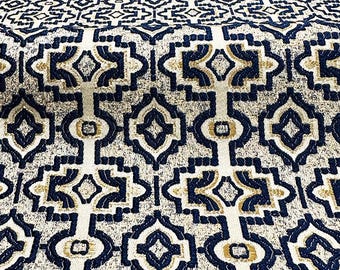 May include: A close-up of a fabric with a geometric pattern in shades of blue, gold, and white. The fabric has a textured surface and a repeating pattern of squares and diamonds.