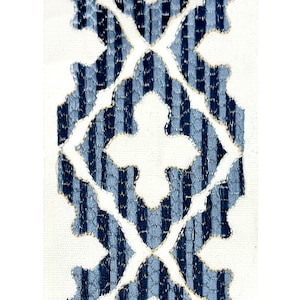 May include: Close-up of a fabric with a repeating pattern. The design features a central vertical band of blue and white striped sections, framed by a white background. The blue stripes have a textured appearance, and the edges are outlined with a gold thread.