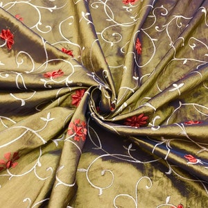 May include: A gold fabric with a white embroidered floral pattern and red flower accents.
