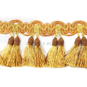 May include: Gold and brown tassel trim with a wavy design. The trim has a fringe of tassels with brown tops and gold strands.