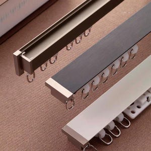 Può includere: Tre bastoni per tende in diverse finiture: argento, nero e bianco. Ogni bastone ha una fila di anelli metallici e un tappo decorativo.